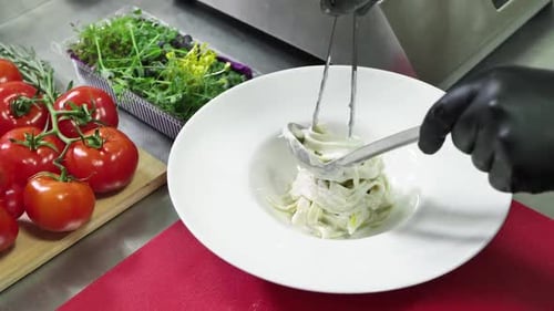 Hands preparing creamy pasta dish in commercial kitchen