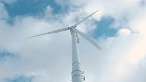 Rotating wind turbine with moving clouds and blue sky in the background.