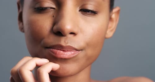 Face, hands and beauty with a woman touching her skin for skincare and wellness in studio on a gray