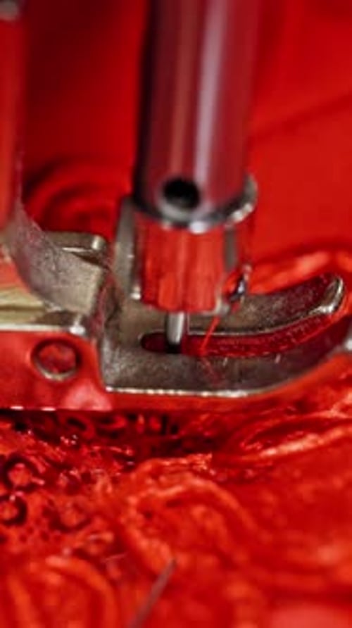 Close-up needle of a sewing machine working on red fabric.