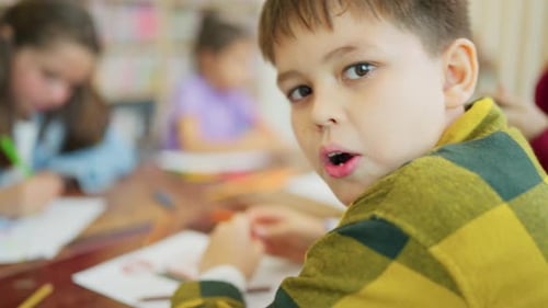 Close up face of young boy who look fun in the class of drawing with his friends in the classroom