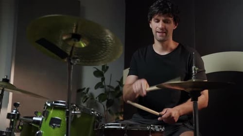 A Young Man Sits Behind a Drum Set in a Home Studio and Plays with Two Drumsticks The Drums are