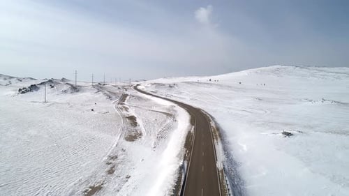 Aerial View on a Road Between the White Snowy Hills Against the Blue Sky