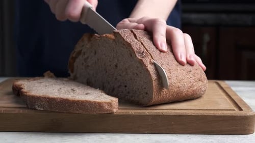 Person Slicing Fresh Bread on Wooden Cutting Board