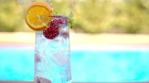 Mojito cocktail glass with ice and cherry and mint, soda and gin near a blue pool close up