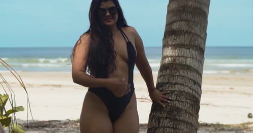 Sexy chica hispana abraza el tronco de un cocotero mientras usa un bikini de tanga en este lugar de playa