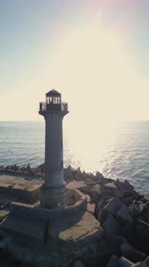 Drone Footage of a Coastal Lighthouse on Rocky Breakwater Scenic Seaside View with Blue Sky Calm