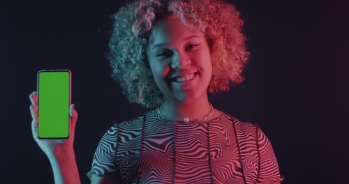 African American Woman Holding Smartphone with Chroma Key Green Screen in Neon Light