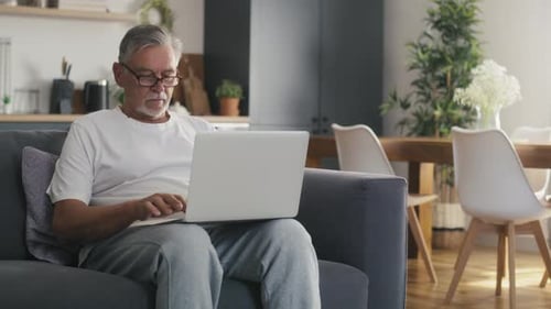 Senior Man Uses Laptop on Couch at Home