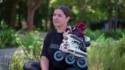 portrait of young smiling hipster girl in skate park holding roller skates in hands before starting