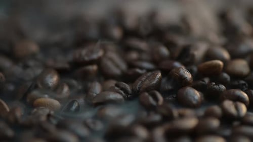 Close-up time-lapse of steaming coffee beans falling, spilling onto the pile of grains
