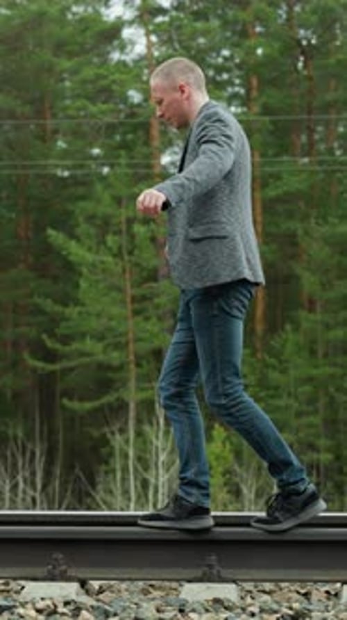 Man Balancing on Railway Tracks in Grey Suit and Blue Jeans in a Serene Forest