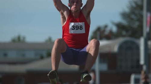 Atleta de atletismo en cámara lenta saltando a la arena en un estadio al aire libre