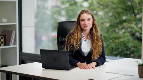 Look Into Camera in a Modern Office with a Large Window a Beautiful Worker in a Blue Shirt with a