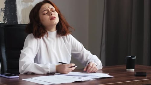 Junge Geschäftsfrau schreibt Artikel oder unterschreibt Papierscheiße, die am Tisch sitzt zerknitterte Papiere auf