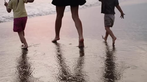 Mother Walking with Her Kids Along the Beach in Ocean Water at Sunset
