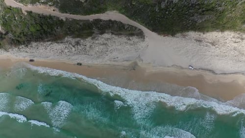 Spinning aerial tracks vehicles on sandy ocean beach in Australia