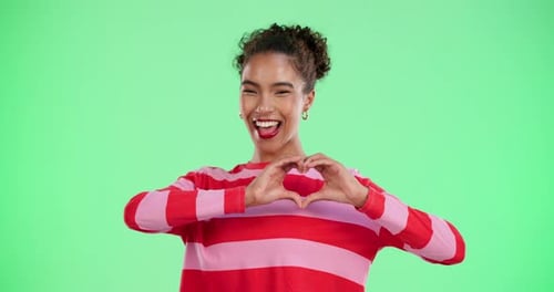 Heart hands, romance and smile of woman on green screen studio for love or valentines day