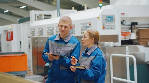Two Industrial Workers in Blue Uniforms Engage in a Collaborative Discussion While Reviewing