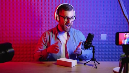 Young Smiling Blogger Unpacking Box with Present Sitting at Home Studio