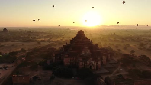 Ancient Buddhist temple in Bagan, Myanmar with dozens of hot air balloons in background during sunri