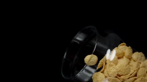 Time for a healthy breakfast with cornflakes. I slowly pour them from a transparent jar. Close-up