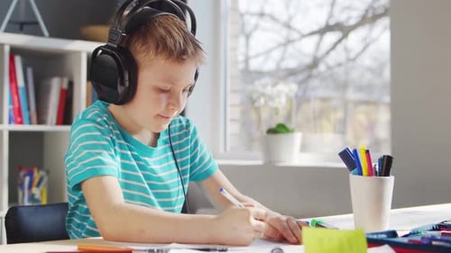 Boy Wearing Headphones Drawing at Desk Indoors
