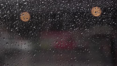 Nahaufnahme von Regentropfen mit vorbeifahrenden Autos im Hintergrund