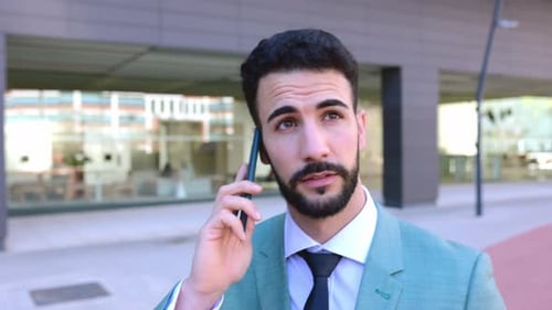 Successful Young Businessman Talking on Mobile Phone While Walking in the Street
