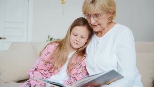 Granddaughter and Grandmother Reading Book Together at Home