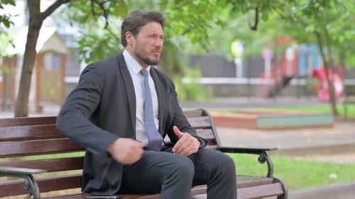 Man in Suit Experiencing Back Pain on Park Bench
