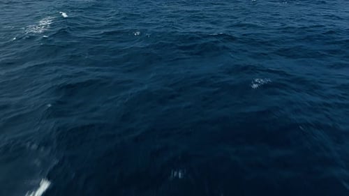 Bird's eye view of open ocean water soaring above shimmering depth of dark blue seas