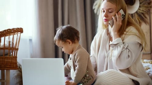 Pretty Young Single Mom Working at Home on a Laptop Computer While Holding Her Baby Girl