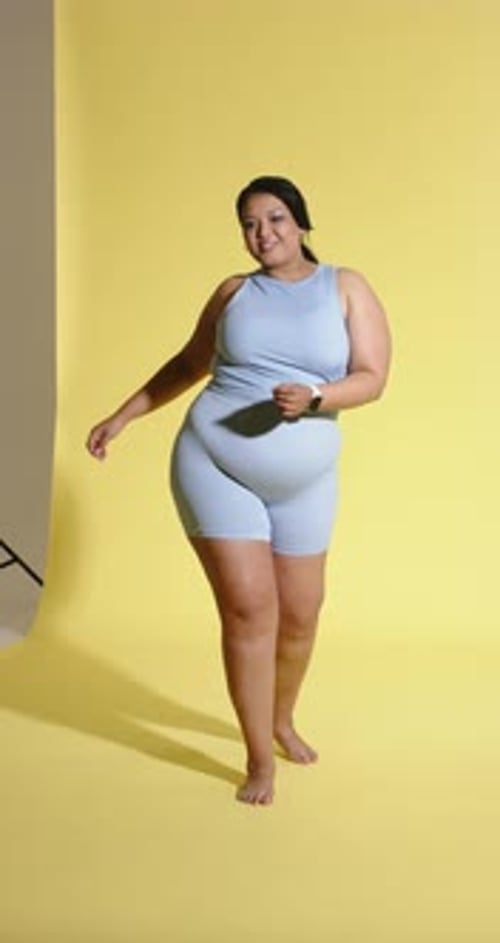 Vertical video: Track starting African American woman dancing on yellow backdrop in studio