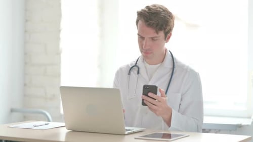 Young Doctor Using Smartphone While Using Laptop in Clinic
