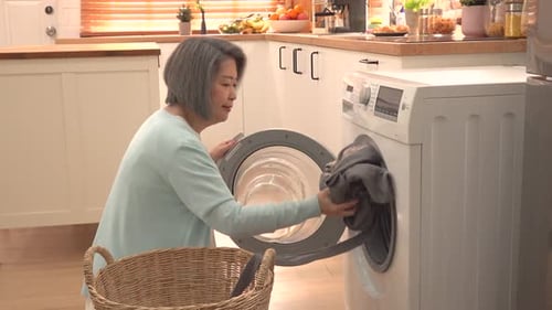 Woman Loads Clothes Into Washing Machine At Home