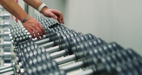 Closeup of a Male Hand Picks Up Dumbbell From the Rack in Gym