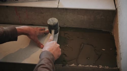 Worker Smooths Adhesive to Install Tile
