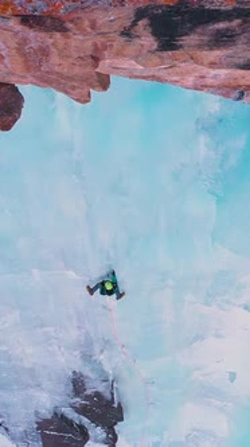 Man is Leading on Ice Ice Climbing on Frozen Waterfall Aerial View Vertical Video