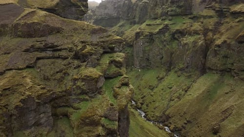 Aerial shot of steep, moss-covered cliffs towering over a narrow canyon with a river flowing through