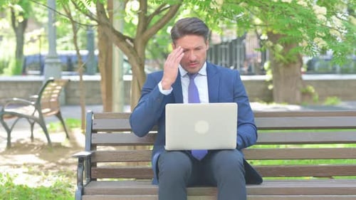 Man Working On Laptop Has Headache In Park