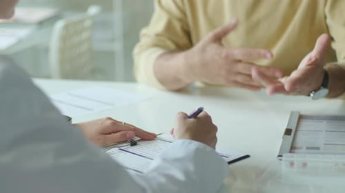 Hands of Female Doctor Interviewing Patient and Writing Medical Records