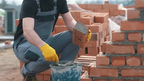 Construction Worker Applying Mortar to Brick With Trowel