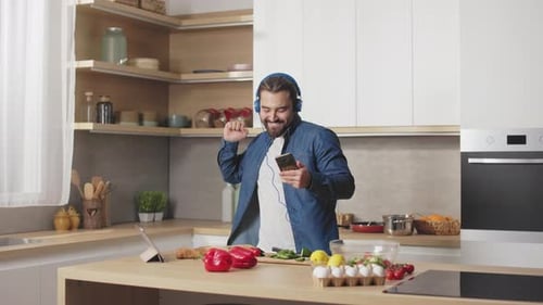 Man Dancing in Kitchen with Headphones and Phone