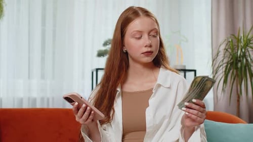 Woman with Money Using Mobile Phone at Home