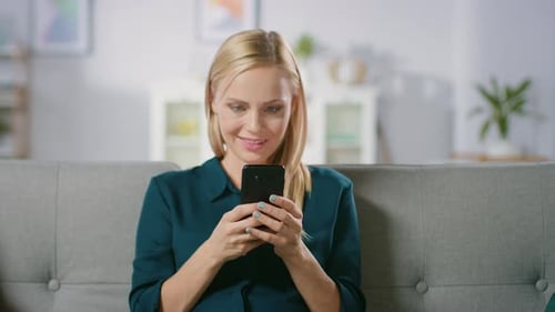 Smiling Woman Using Smartphone on Sofa at Home