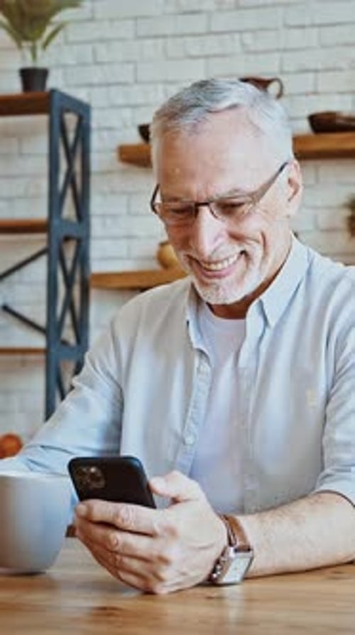 Senior Man Using Phone and Drinking Coffee Indoors