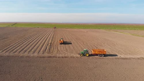 Drone shot of tractors, farmers working on brown, earthy farmland, plowing and harvesting