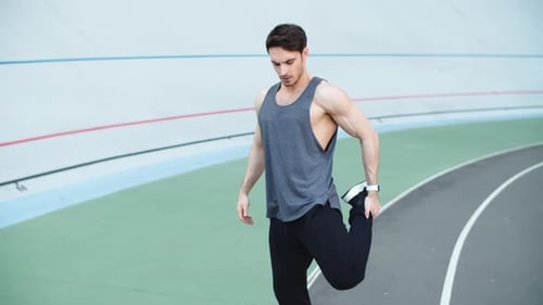 Muscular Man Stretching Legs at Stadium. Man Runner Warming Up Before Workout