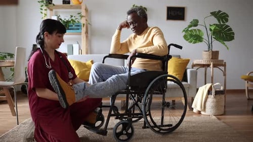 Caregiver Assists Senior Man with Leg in Living Room